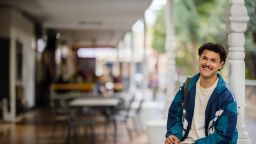  A student smiles while sitting outdoors on campus, enjoying a relaxed moment between classes.