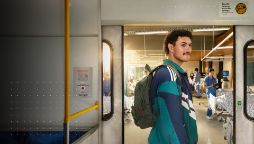 A student standing inside a train carriage, with a hospital room just outside the doors.