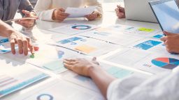  table with reports with different charts and diagrams with people hands on top of some papers