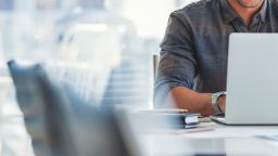 Male torso in grey shirt behind a laptop screen.