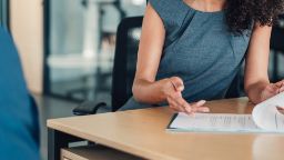 Business professional woman in a grey dress sitting at a table discussing a contract on the table
