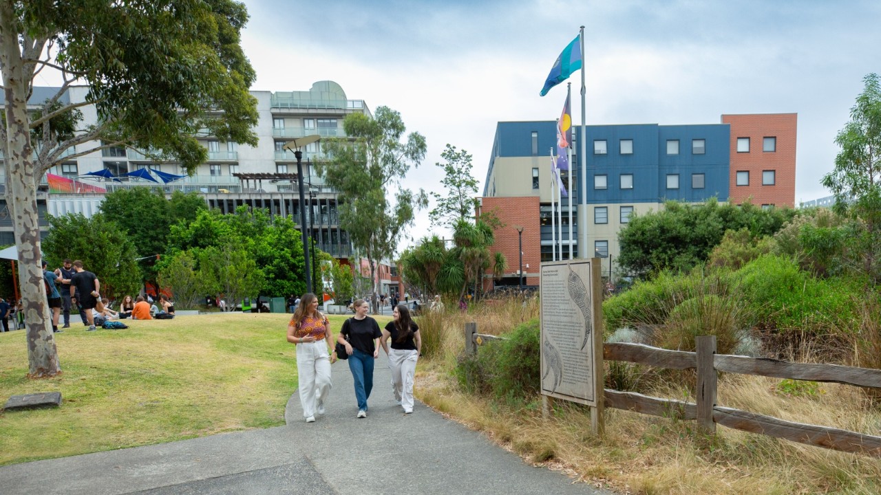 Three Indigenous students walking alongside the Aunty Dot Peters AM Flowering Grassland on Swinburne's Hawthorn campus.