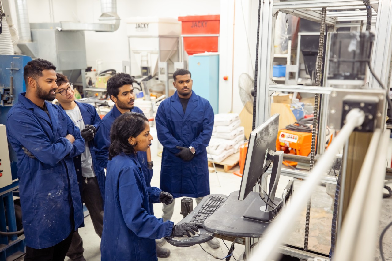 Students standing around a computer next to a concrete 3D Printer in the Digital Construction Lab.