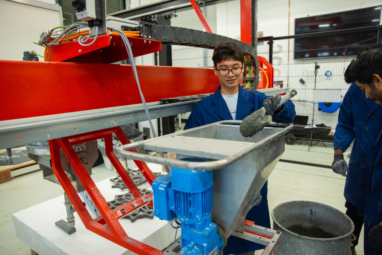 Students shoveling concrete into the integrated concrete mixing system for a large-scale 3D concrete printer