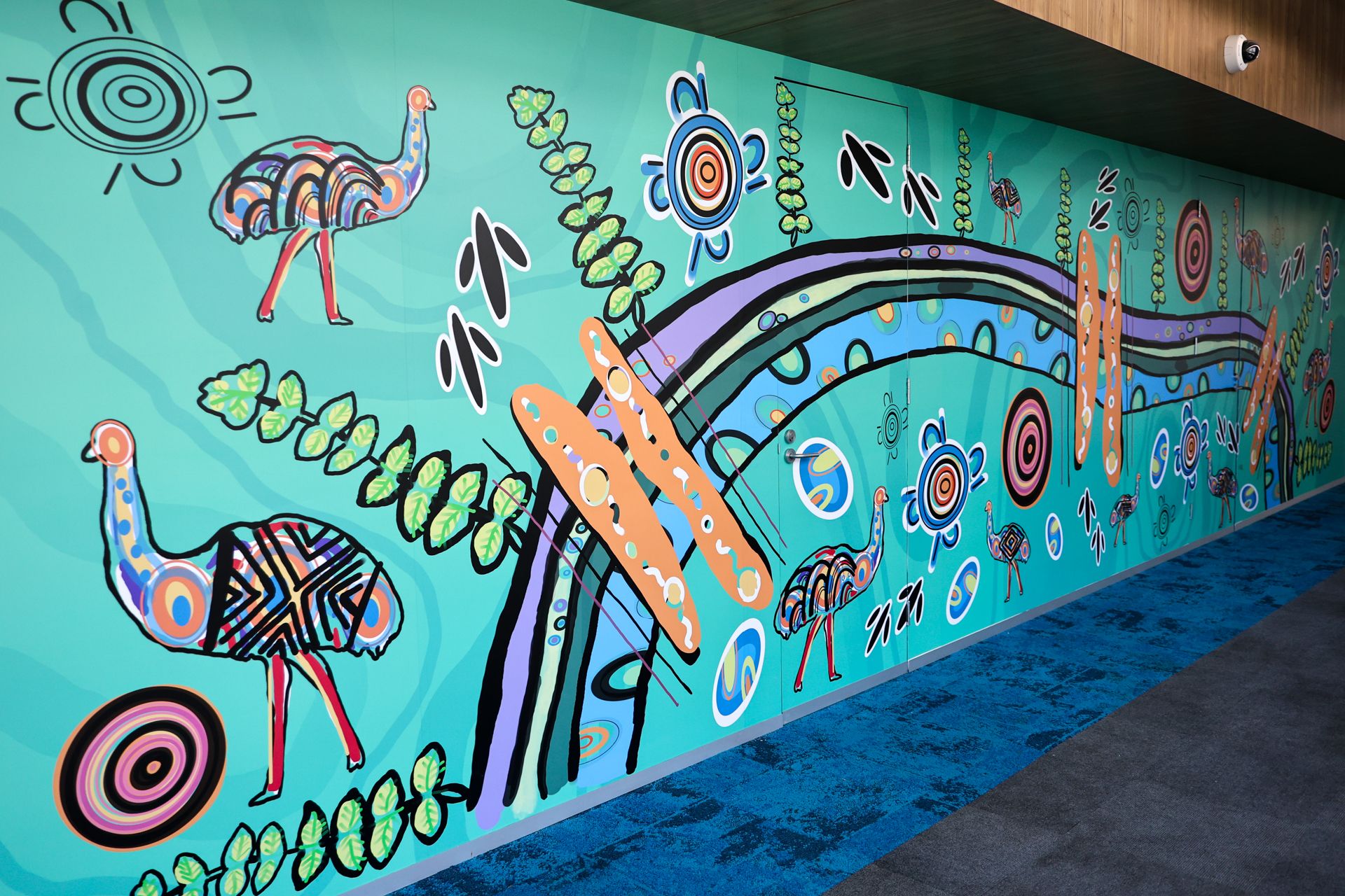 Indigenous artwork by Mandi Barton, featuring emus, bright colours and flowing lines along a wall. 