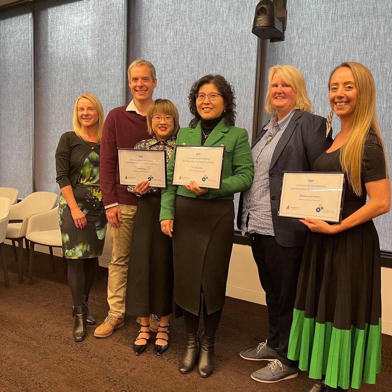 Six people standing at a window showing off their awards. 