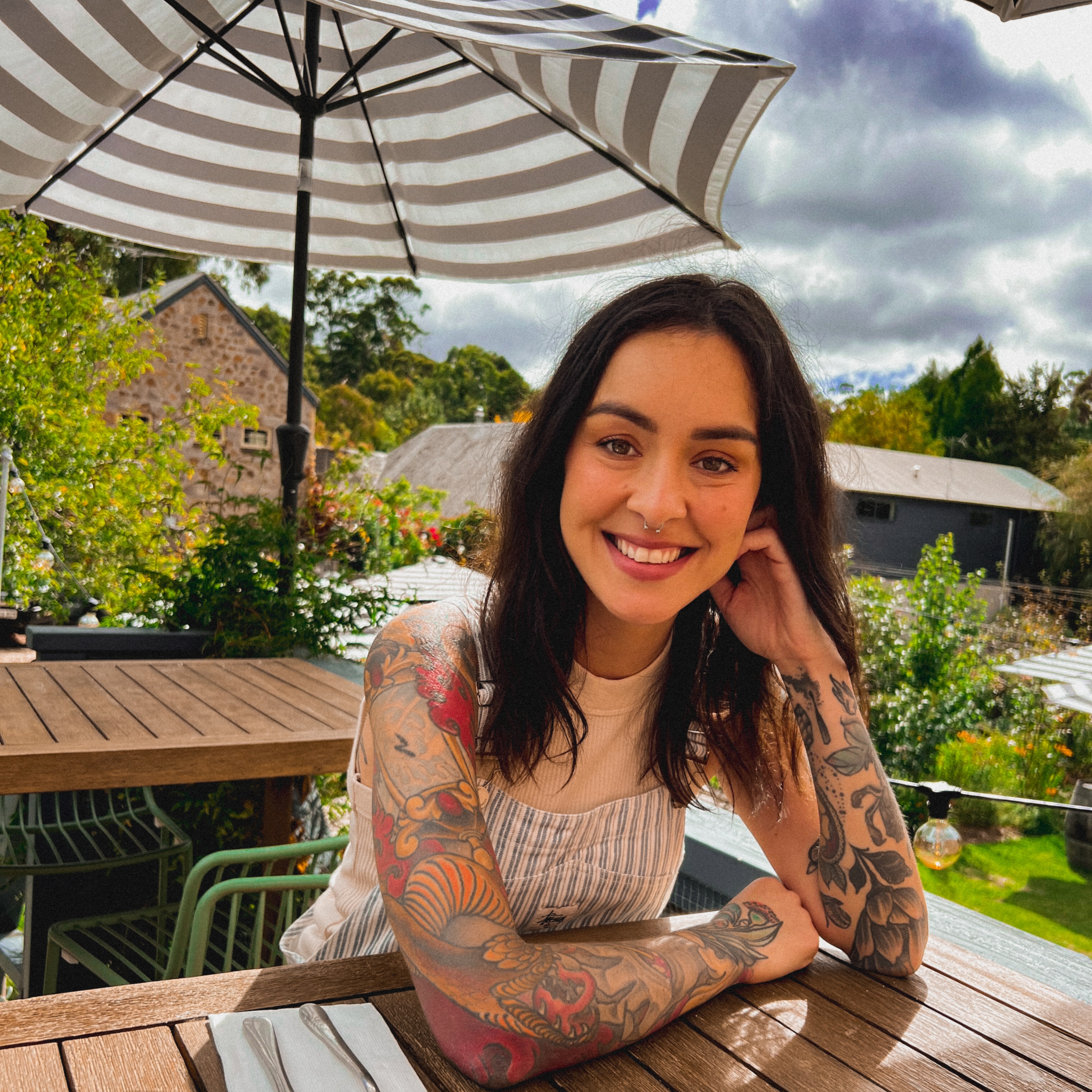 Young lady sitting at a table on a patio at a restaurant, smiling at the camera. 
