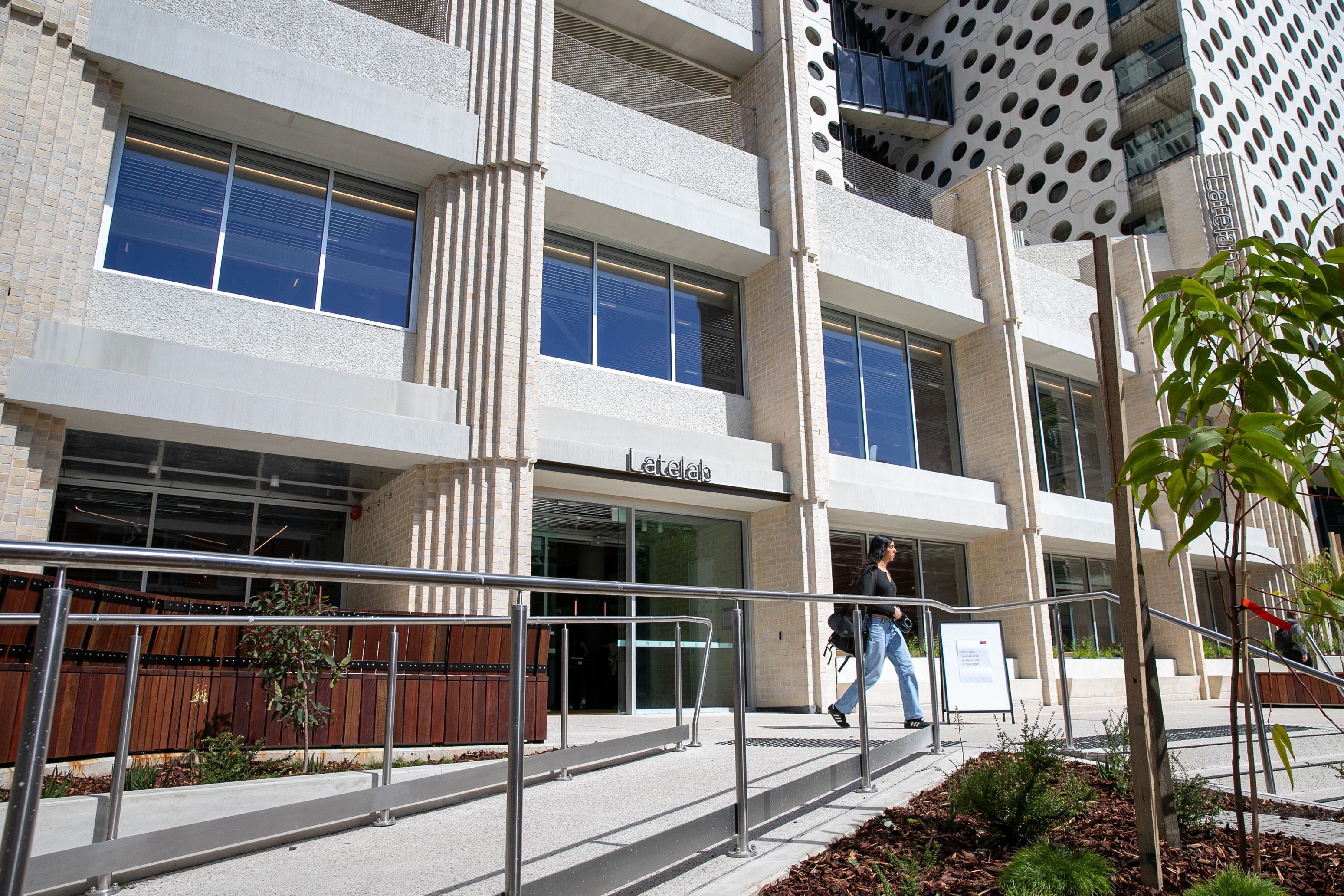 A young women walking with her shoulder study bag past a new study building