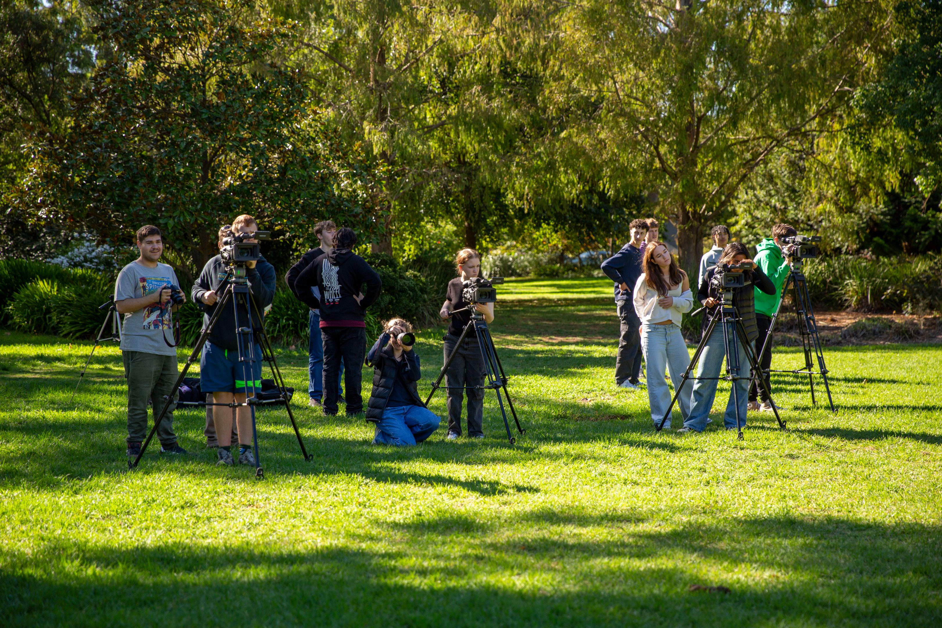 13 students practicing with film and photography cameras in a park. 
