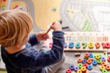 A toddler playing with colourful wooden shapes and numbers
