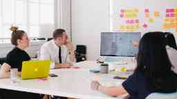 A group of people sitting in a workshop looking at a screen, with post-it notes on the background wall.