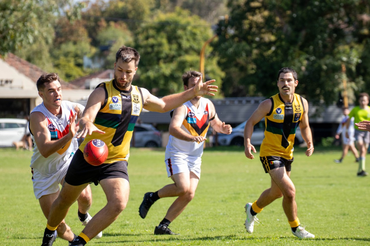 AFL amature game, with a player kicking the ball, and the opposition running towards them at the end. 