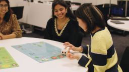 Three Education students sitting around a table in classroom testing robot learning tool