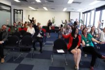 A group of event attendees sitting in rows of chairs all smiling and waving. 