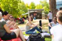 A group of male and female students sit on the grass in the sun during o week
