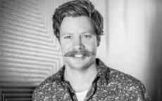 Black and white image of Jesse Leeworthy smiling to camera in a patterned shirt