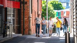 Group of 5 students chatting and walking together down McLeod Lane, between AMDC and FS buildings