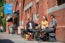 Wide shot - 3 students sitting and talking while drinking coffee on Don Street near Glenferrie Station