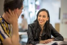 Medium close up of female student talking to and smiling at other student in FS building