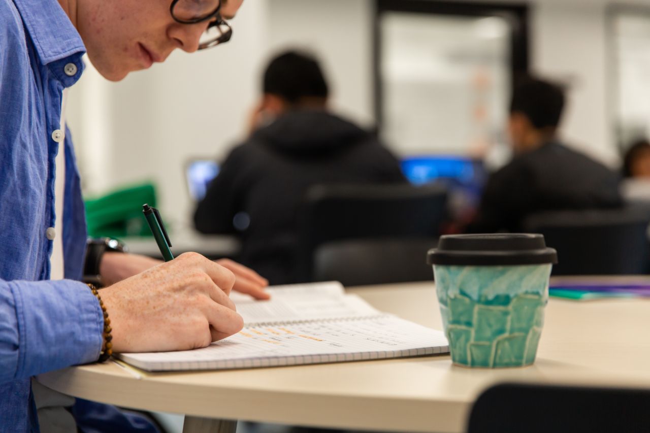 Close up of a person at a table writing in a notebook 