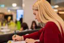 A female student wearing a red jumper writes on a paper form