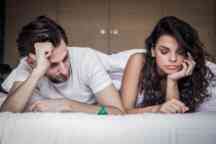 Male and female  lying on a bed contemplating the use of condoms.