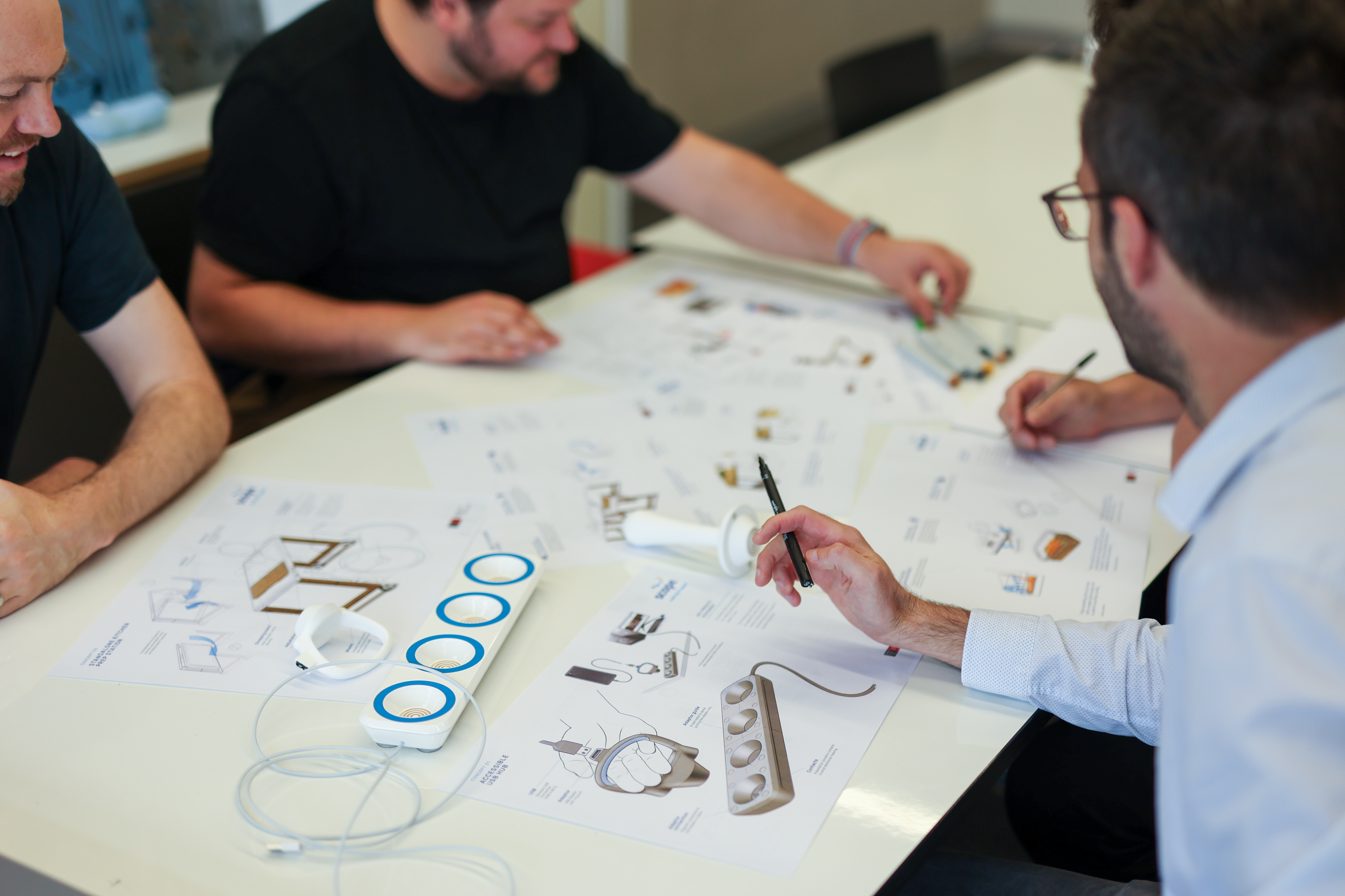 Four CDI members sit around a table with mockup illustrations, markers, and a prototype USB hub