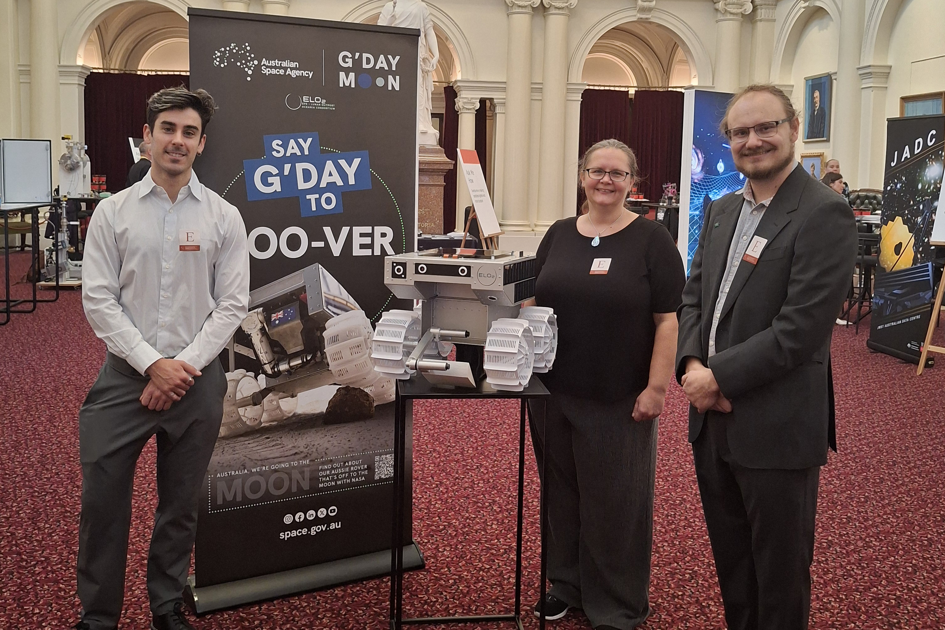 Swinburne researchers Daniel Ricardo, Michelle Dunn, and Philipp Zanon stand with the model of Roo-ver, Australia's lunar rover, at Victorian Parliament House.