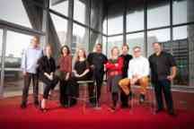 Group photo with five men and four women of varying ages and races standing or sitting in a row