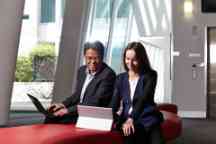 An Asian man and caucasian female in suits looking a laptops in an office setting