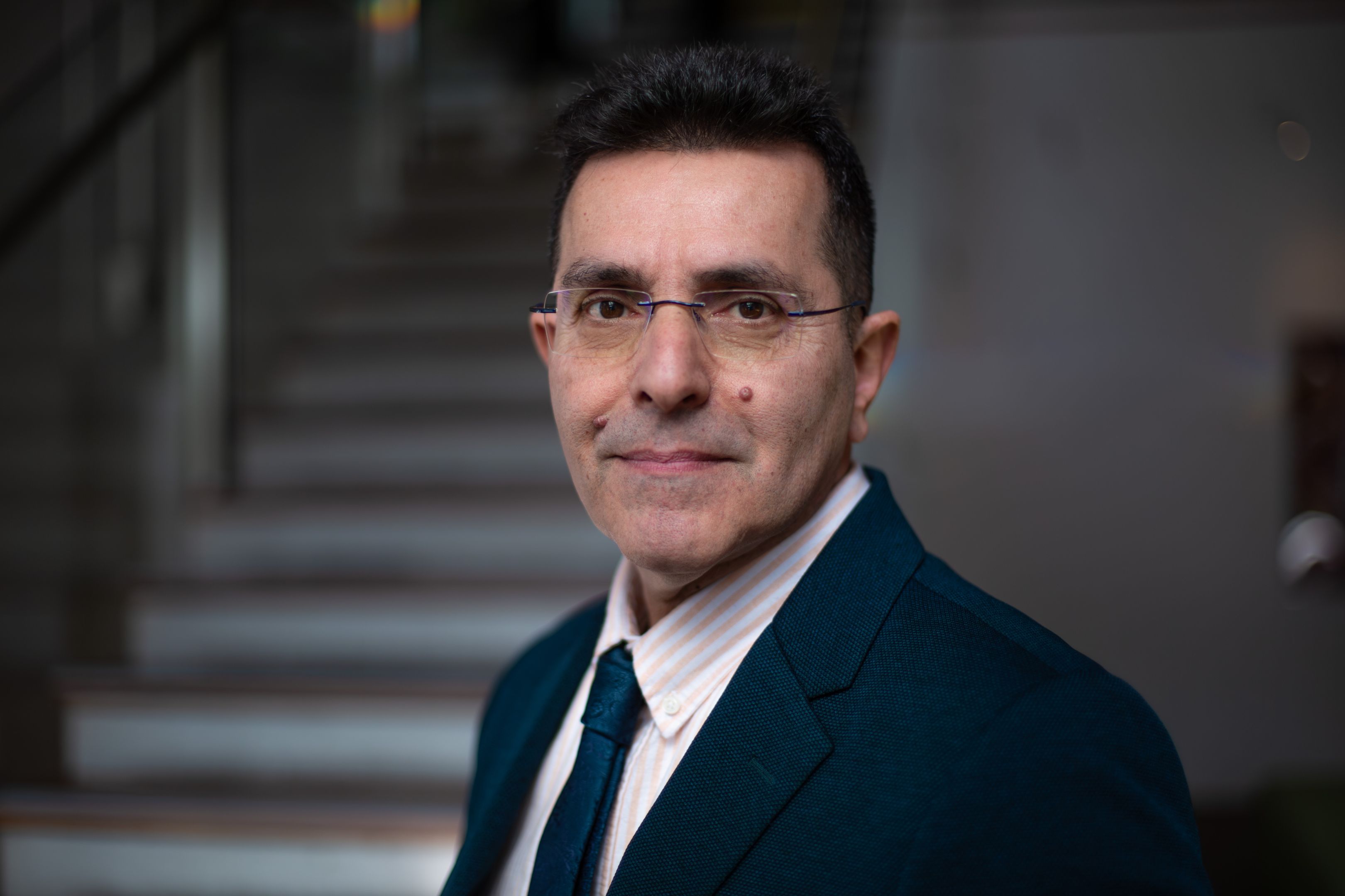 Man with glasses in a suit  standing slightly side on looking at the camera.