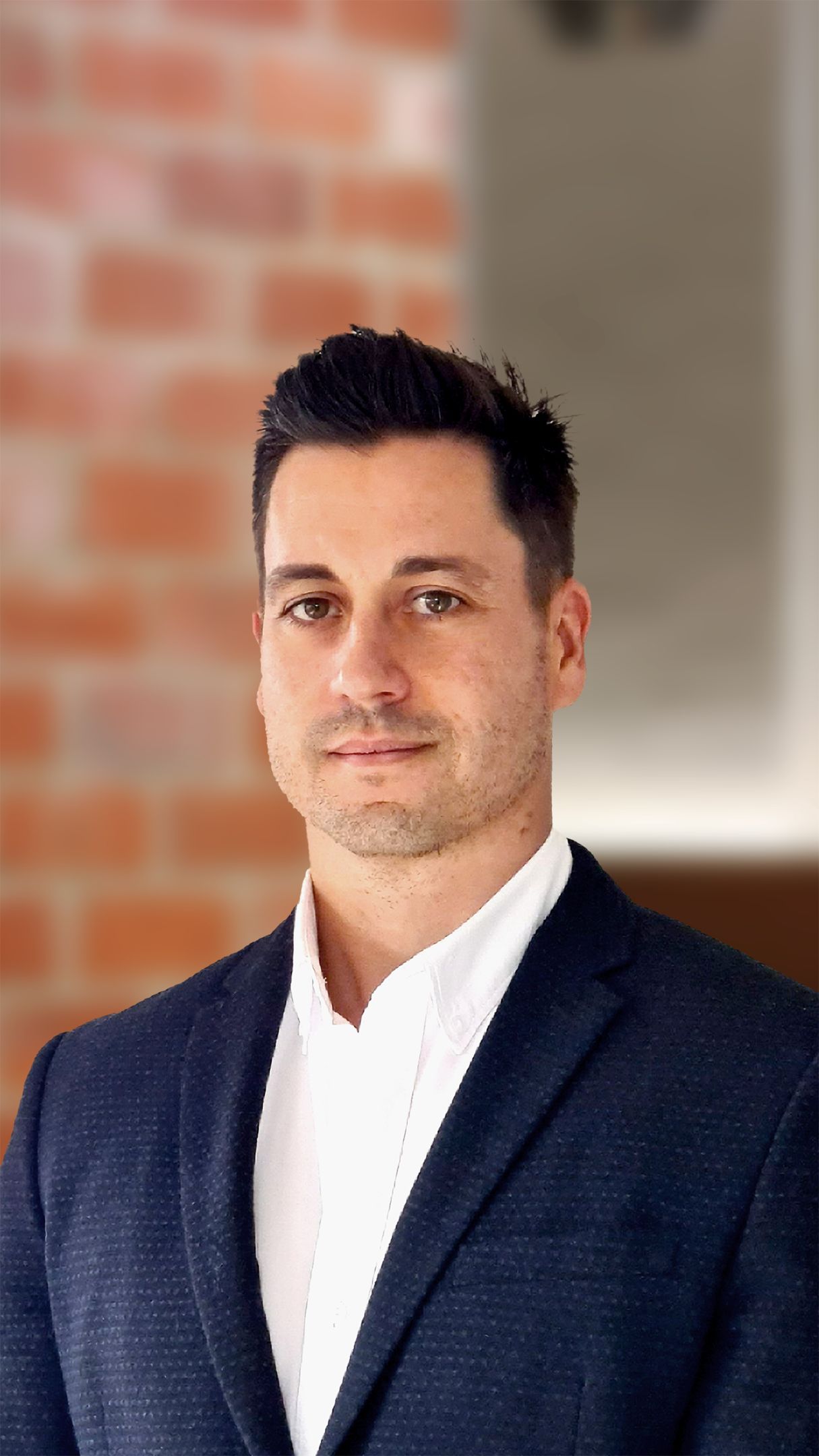 Man with brown hair in a suit smiling, posing for the camera.