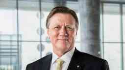 A professional looking man wearing a suit, smiling at camera in front of a glass wall.