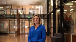 Genevieve Lazzari poses with hands clasped out in front wearing a blue shirt on the ground floor of the AMDC building