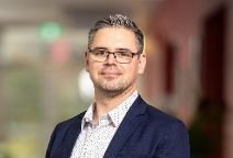 Man with glasses looking at the camera, wearing professional attire.