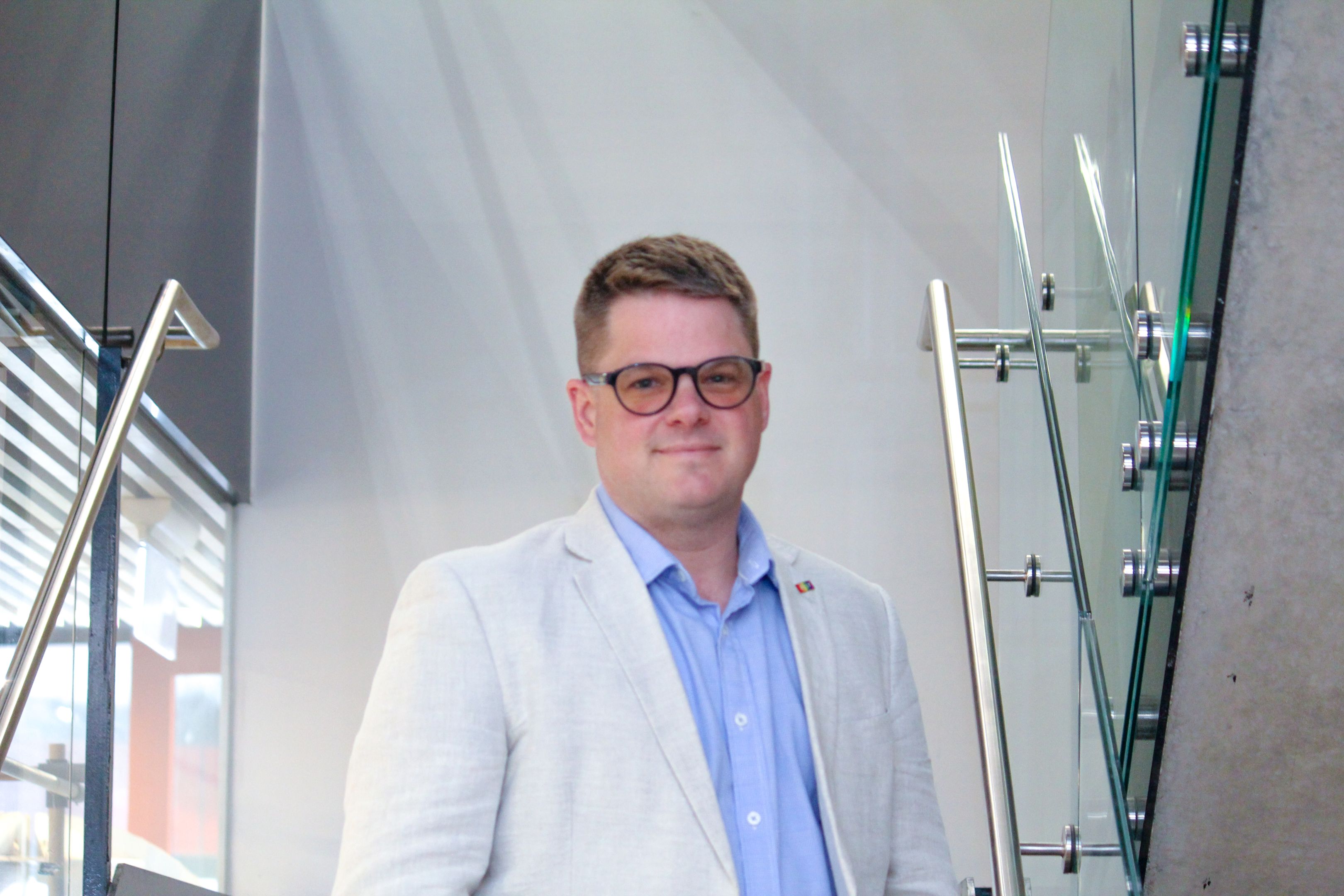 Swinburne Staff Member Llew Mann standing on a set of concrete stairs with a glass railing and a white wall behind. 