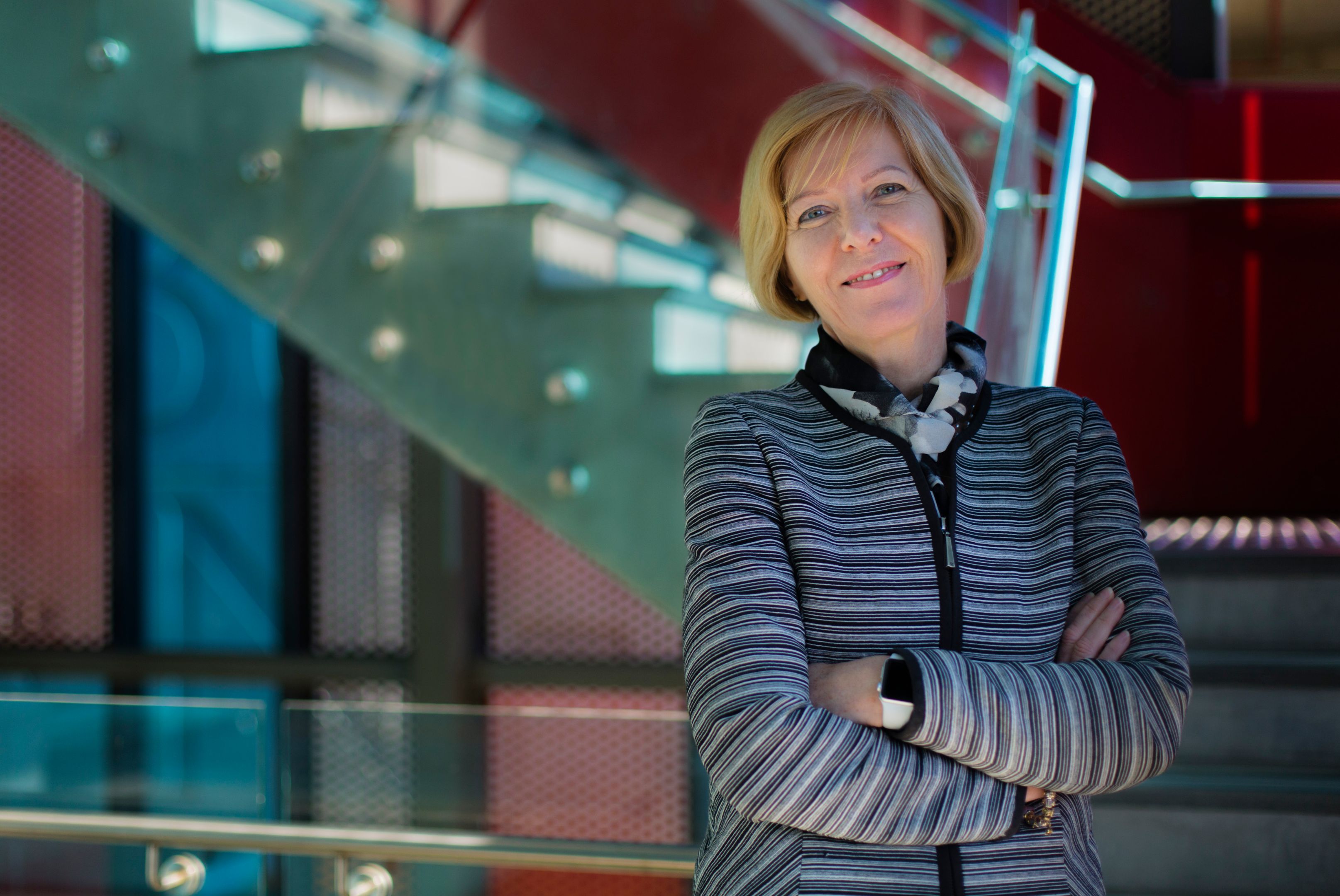 Swinburne Vice-Chancellor Pascale Quester smiling with arms crossed wearing a striped cardigan in front of a stairwell