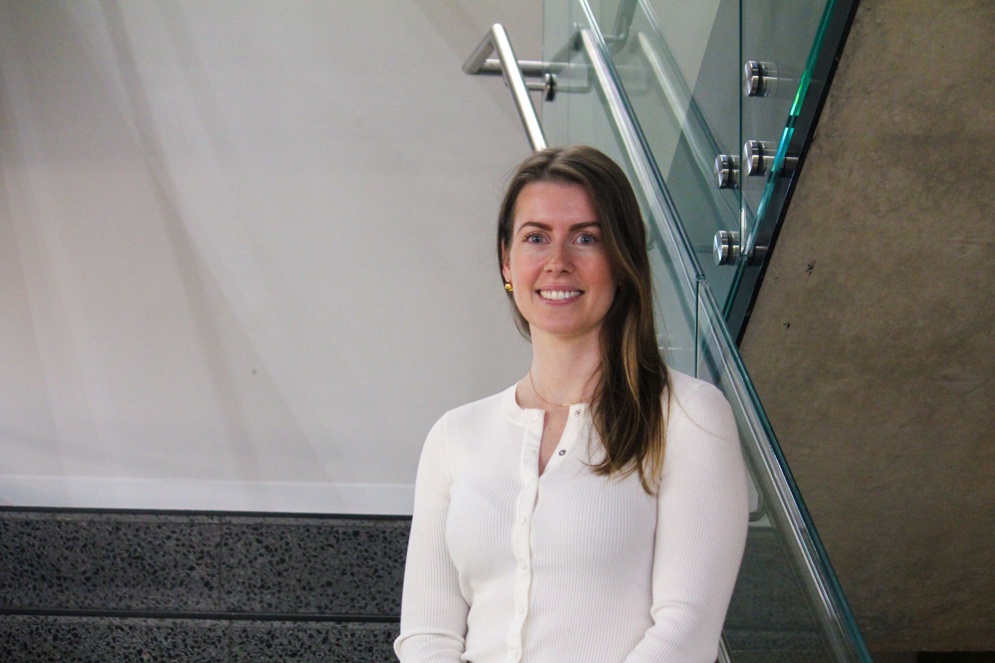 Swinburne Staff Member Yvonne Newell standing on a set of concrete stairs with a glass railing and a white wall behind. 