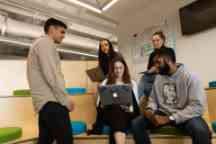 A group of male and female students sit on benches and discuss an assignment 