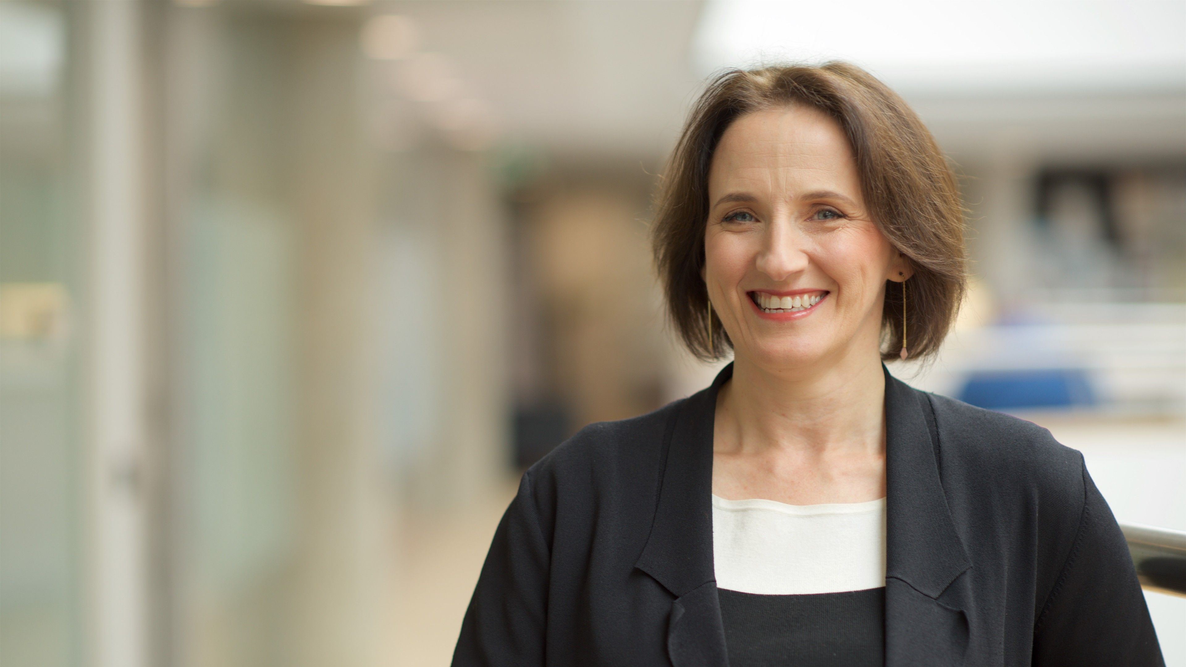 Professional female smiles to camera at the AGSE building wearing a black blazer 