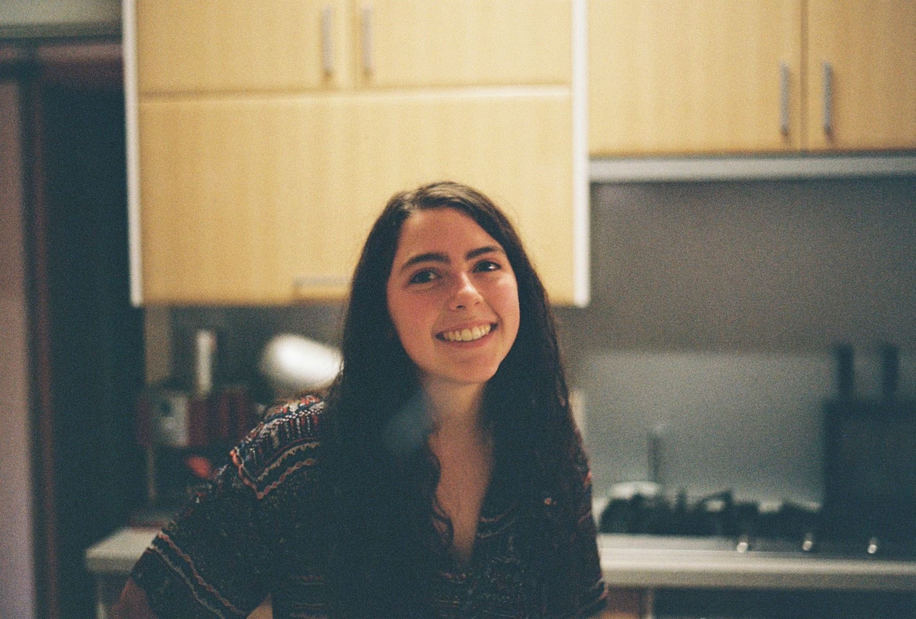Claudia, a young female student with brown hair, standing and smiling in a kitchen.