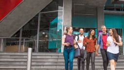 Group of male and female students walk out of The George building chatting and smiling after a class