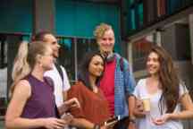 Students socialise outside a building in Hawthorn campus holding books, phones, and coffee cups
