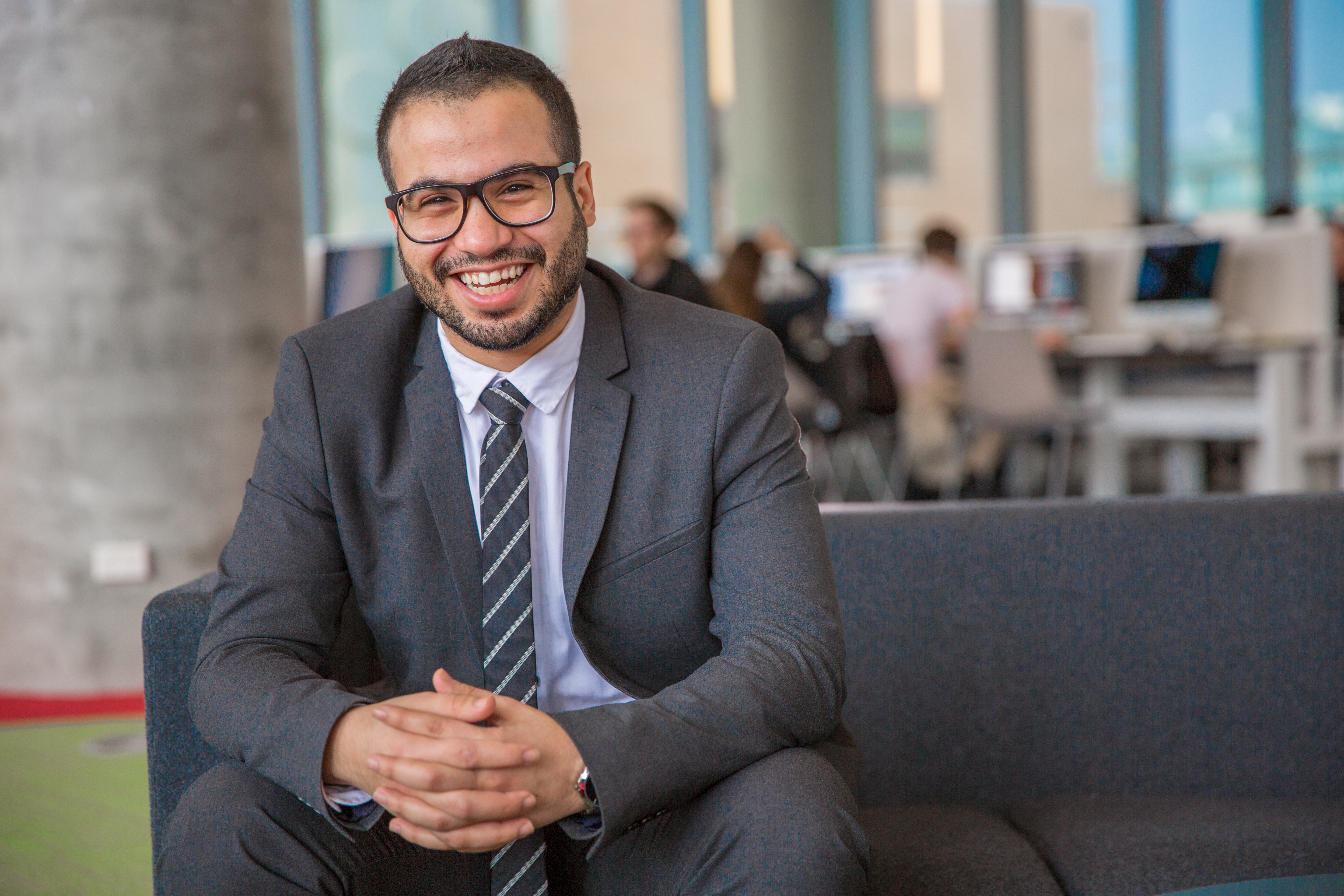Male IT student sits and smiles to the camera wearing glasses and dressed professionally