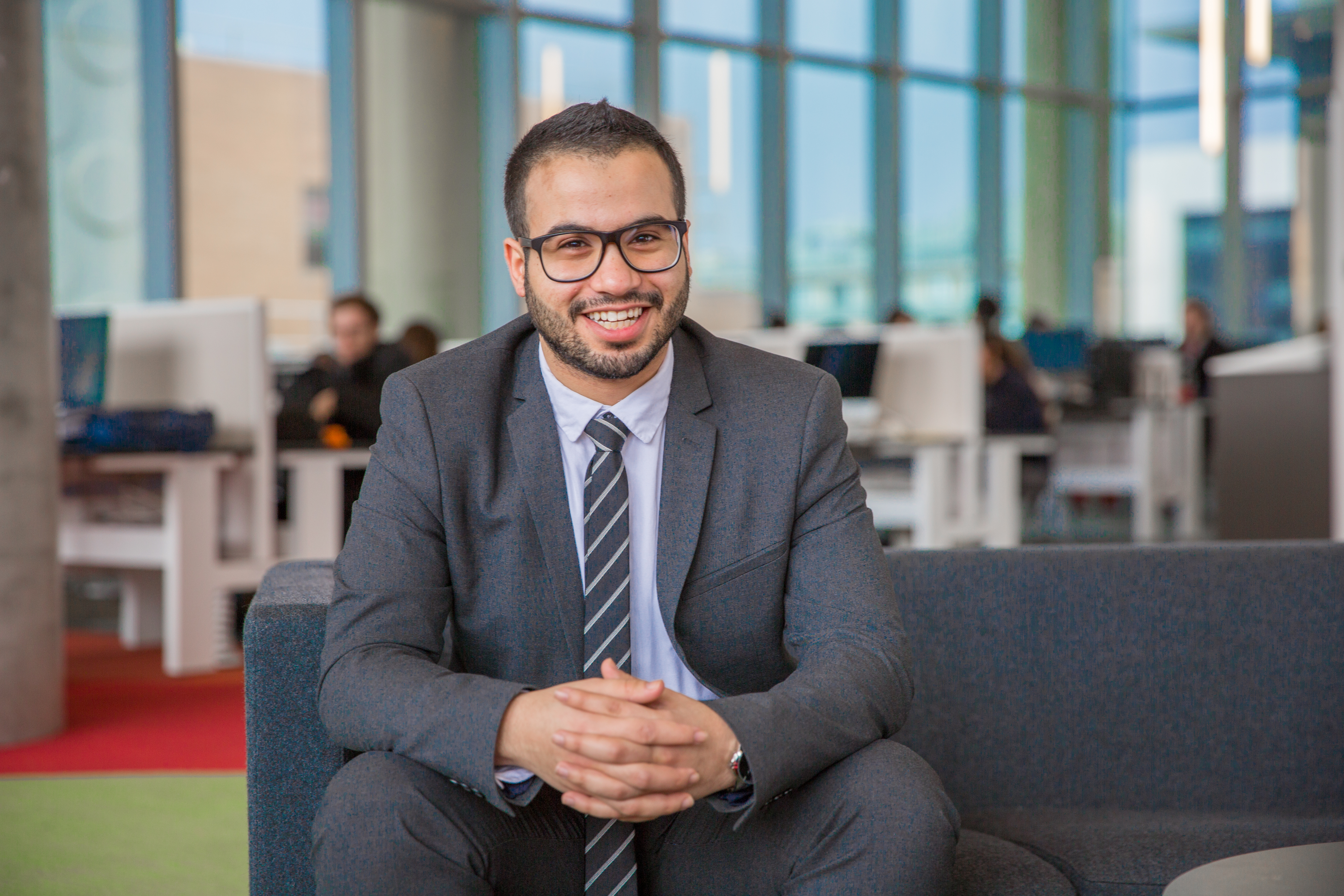 Male student professionally dressed in a suit sits and smiles to camera