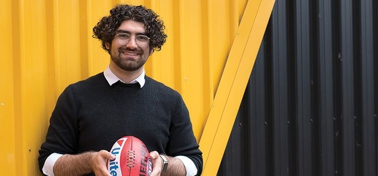 Swinburne design student,. Osama, holding a football outside Richmond Football Club as part of his internship experience.
