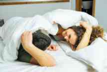 Young happy couple fully clothed under the covers, smiling and enjoying an intimate moment.