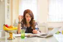 Teenage girl studying using books and laptop at home.