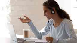 Side view head shot of a smiling mixed race female wearing a headset, with laptop communicating via video chat. 