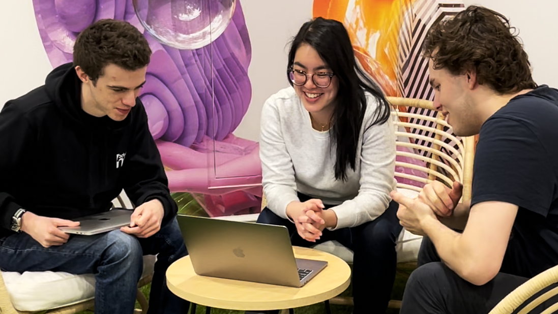 Three people sit around a laptop looking at the screen